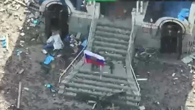 Российский военный демонстрирует флаг РФ на руинах дома