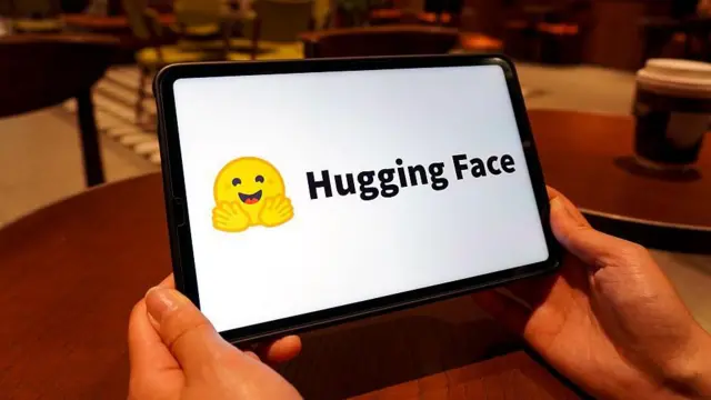 Hugging Face标志显示于平板电脑萤幕上。该标志是一个黄色笑脸表情符号,双手向前张开。