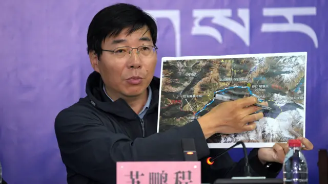 西藏吉隆镇新闻发布会现场,中国科学院成都山地所研究员苏鹏程举起一张卫星照片讲解中方认定的事发经过(中新社图片30/8/2026)