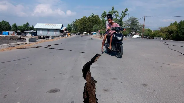 印尼东努沙登加拉省地震后，一名电单车骑士驶过道路裂缝。