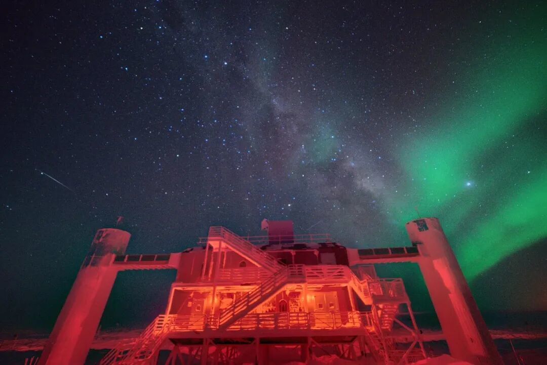 南极冬季夜空下的冰立方实验室，头顶是银河与极光，探测器就埋在它下方的冰层里。丨John Hardin/Wikimedia Commons（CC BY 4.0）