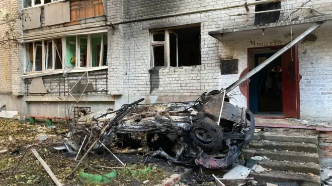 Сгоревший автомобиль на фоне поврежденной многоэтажки
