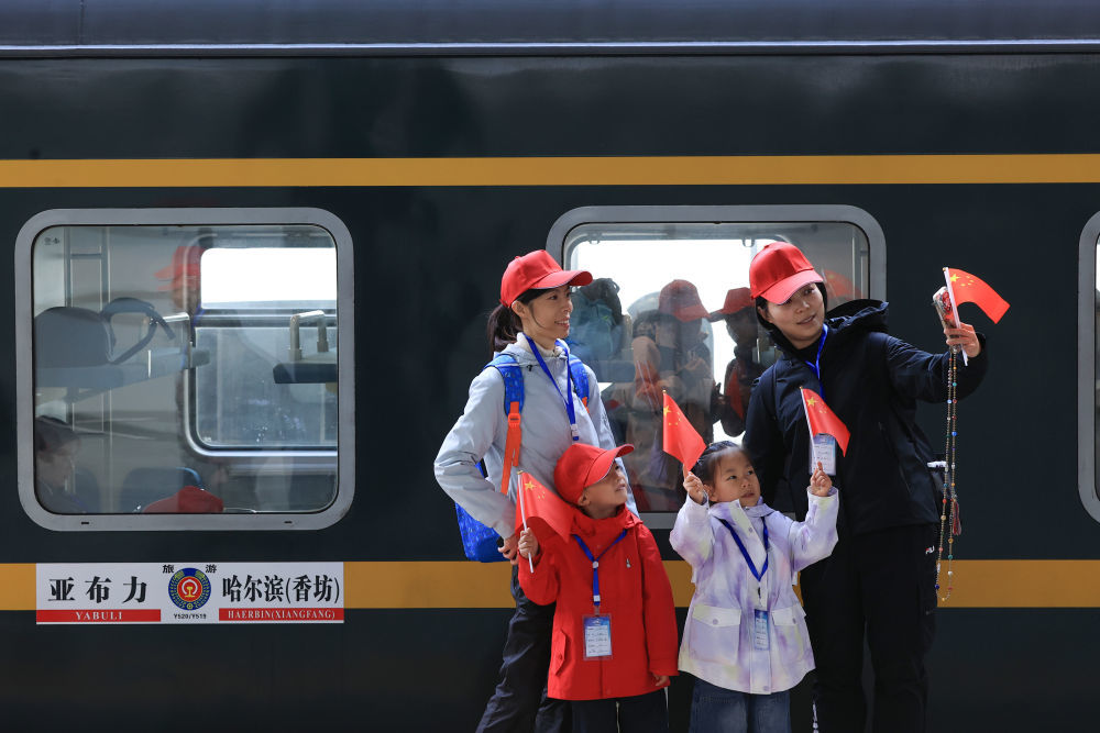 10月1日,旅客在黑龙江哈尔滨站乘车出游前手持国旗合影留念。新华社发(徐率 摄)