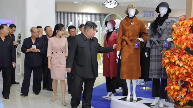 在平壤举行的朝鲜劳动党中央轻工业部全国服装及鞋展上,金正恩(中)与女儿金主爱(左)端详一件女装大衣,干部跟随其后(朝中社图片19/10/2026)