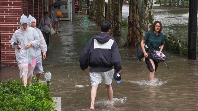 2026年8月9日,在中国上海,居民在白海豚台风带来的暴雨中涉水穿过零陵路被淹没的街道。受台风影响,这座城市出现强风和广泛水浸。
