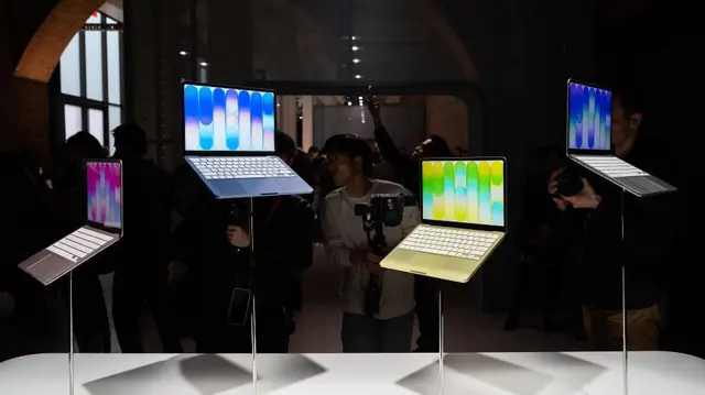 在苹果专门店的展示区内，多部色彩鲜明的 Apple Neo 笔记型电脑以不同高度陈列于展示架上，周围挤满摄影师争相拍摄。