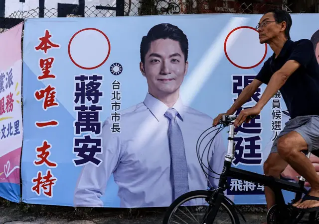 2026年10月15日,台北街头一名男子骑车经过印有国民党台北市长候选人蒋万安肖像的竞选看板。